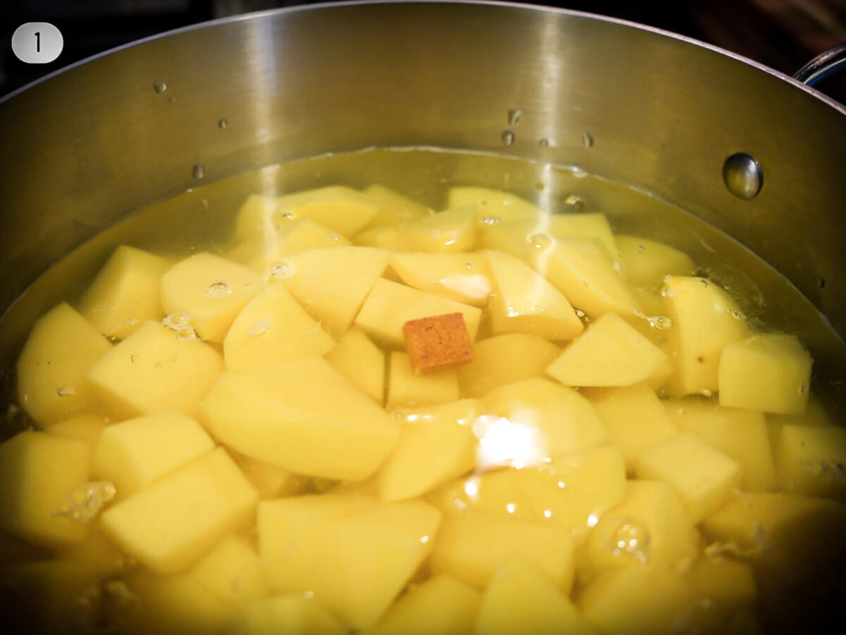 step 1 photo of peeled yukon potatoes in a pot of water with a chicken bouillon cube