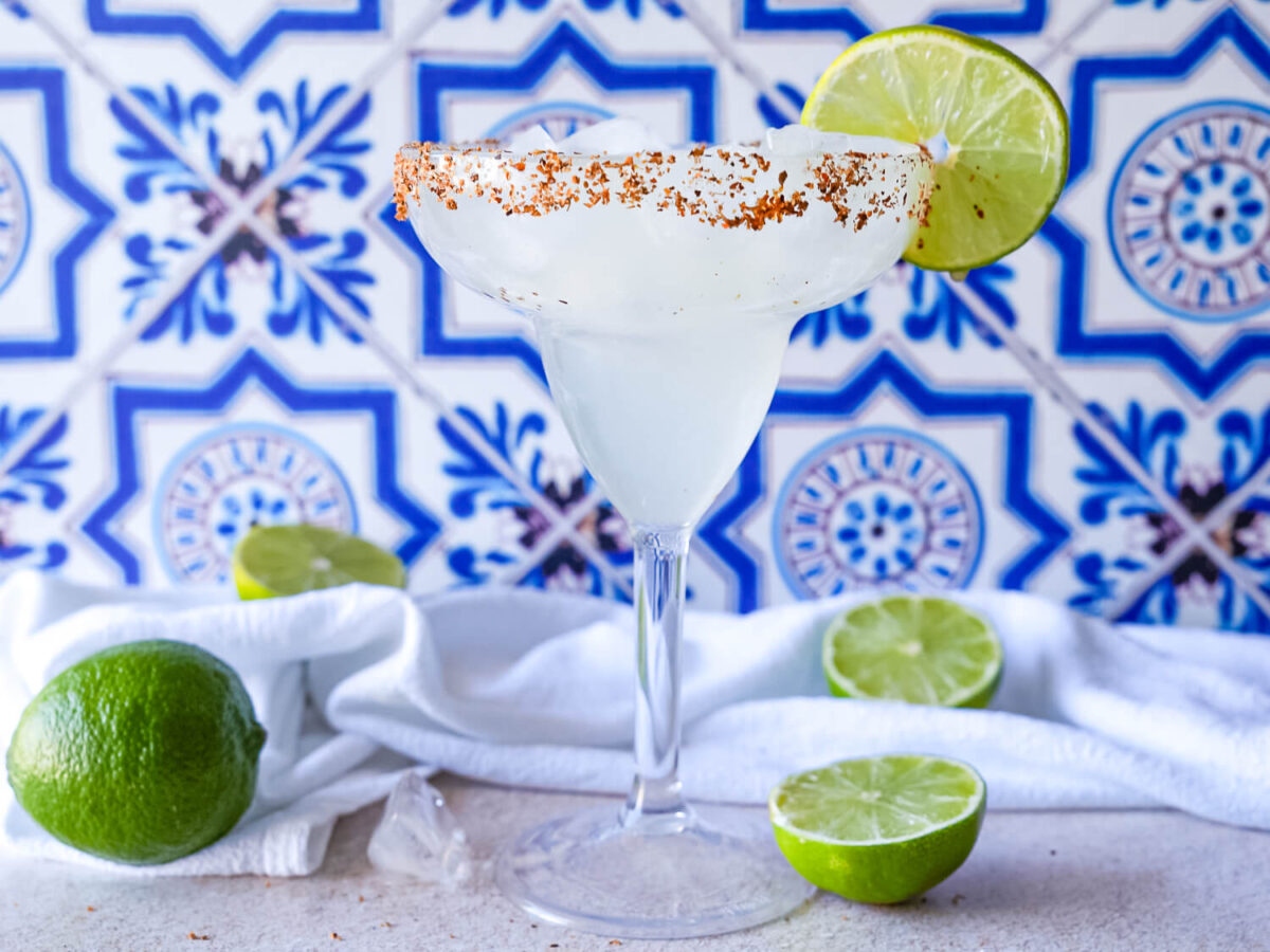 front photo of a full margarita in a glass surrounded by limes