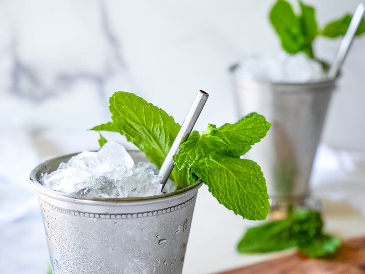 close up photo of a two frosted mint juleps. One is blurred in the background