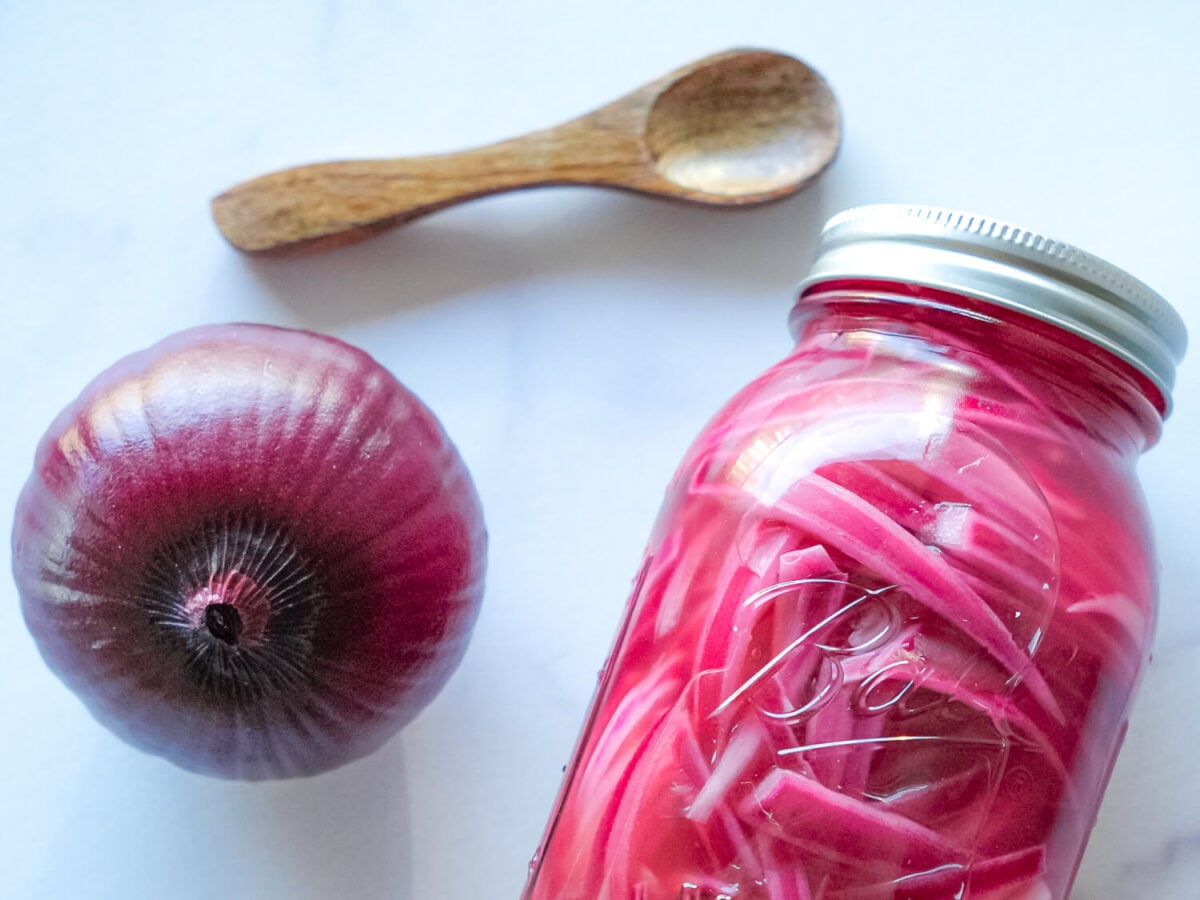 close up photo of pickled red onions on a white surface next to a wooden spoon