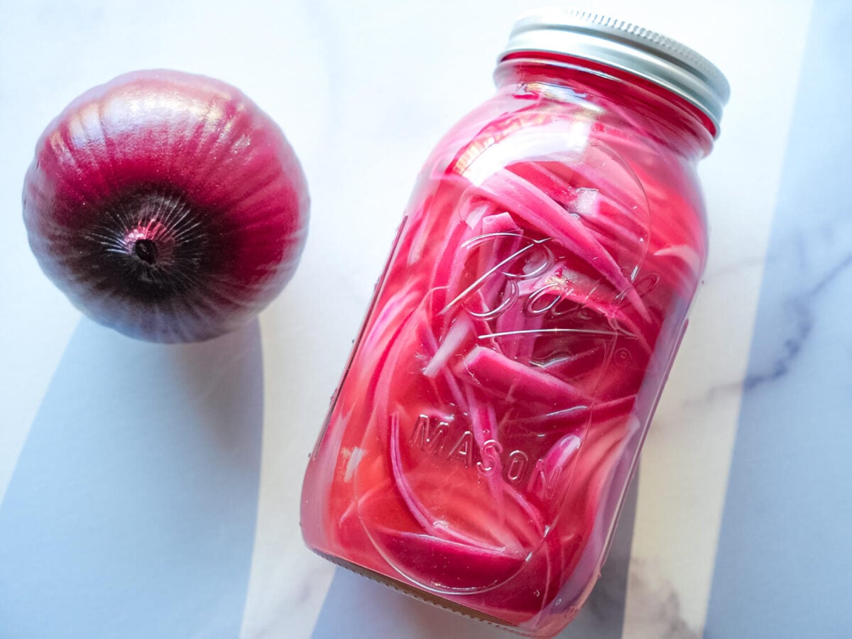 overhead photo of a pickled red onions in a mason jar next to a red onion