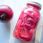 overhead photo of a pickled red onions in a mason jar next to a red onion