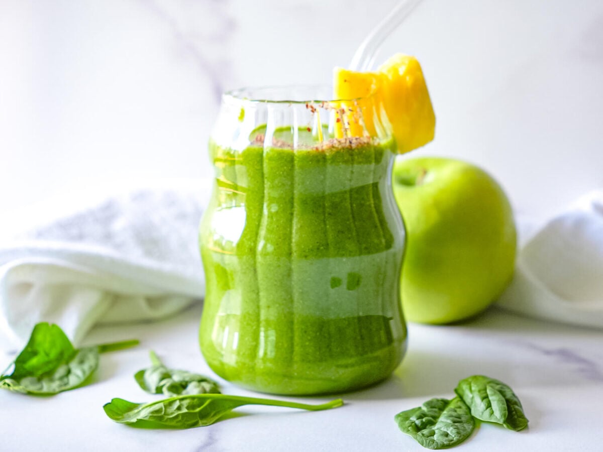 photo of a Pineapple Spinach Smoothie next to a green apple and spinach leaves