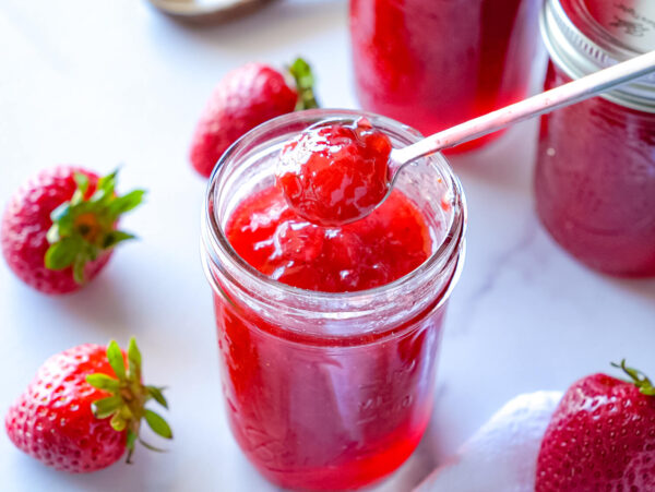 photo of a spoonful of strawberry jam over a mason jar