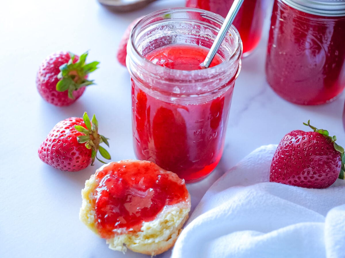 photo of a strawberry jam jar next to a biscuit with strawberry jam on top