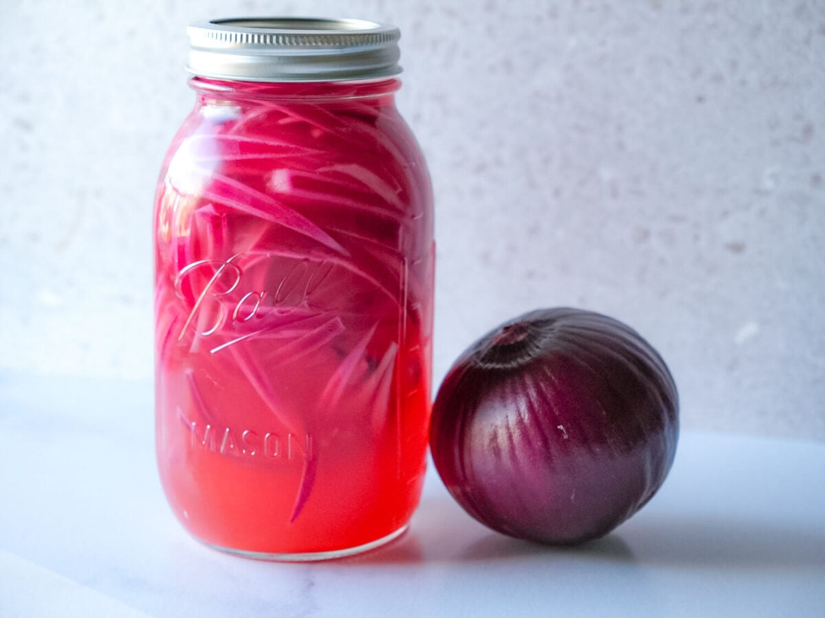photo of pickled red onions in a mason jar next to a red onion