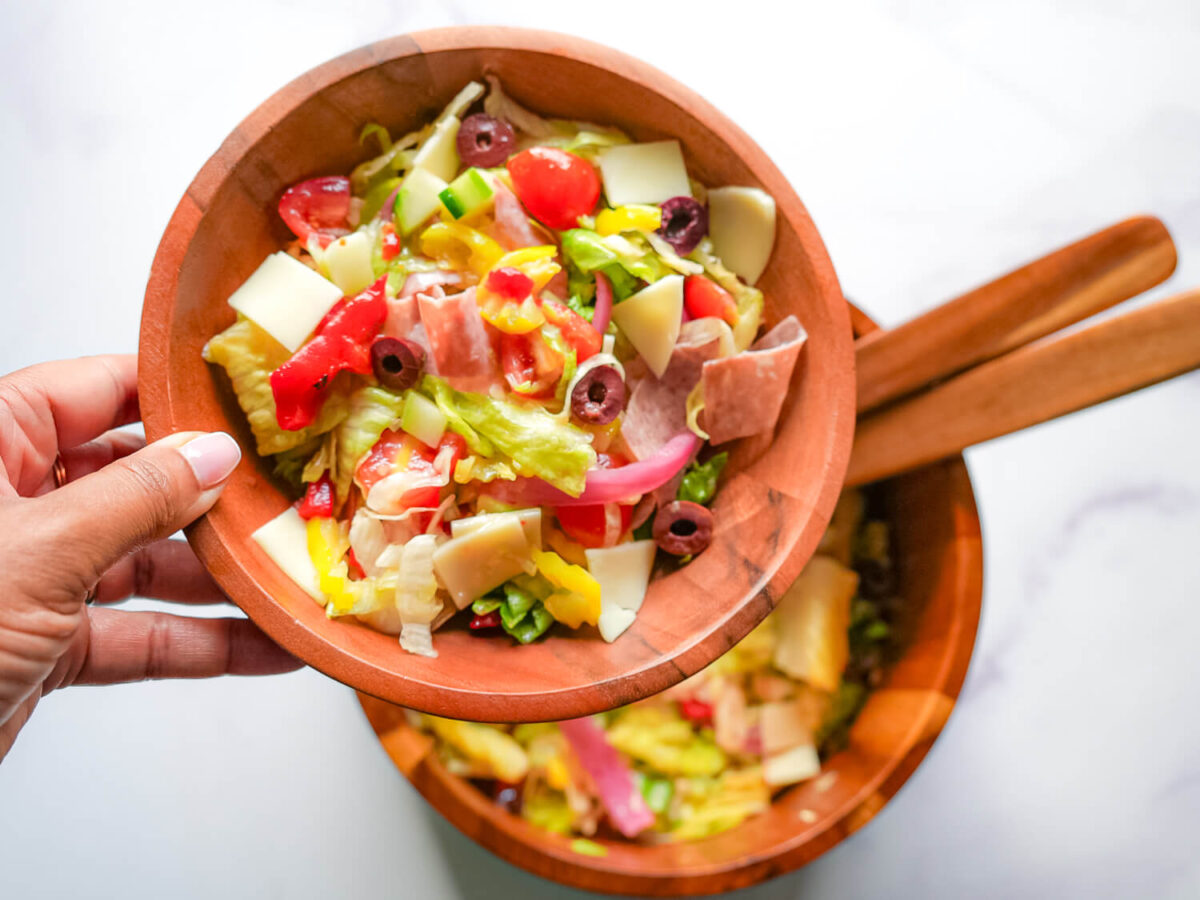 photo of someone holding a wooden bowl full of Italian chopped salad