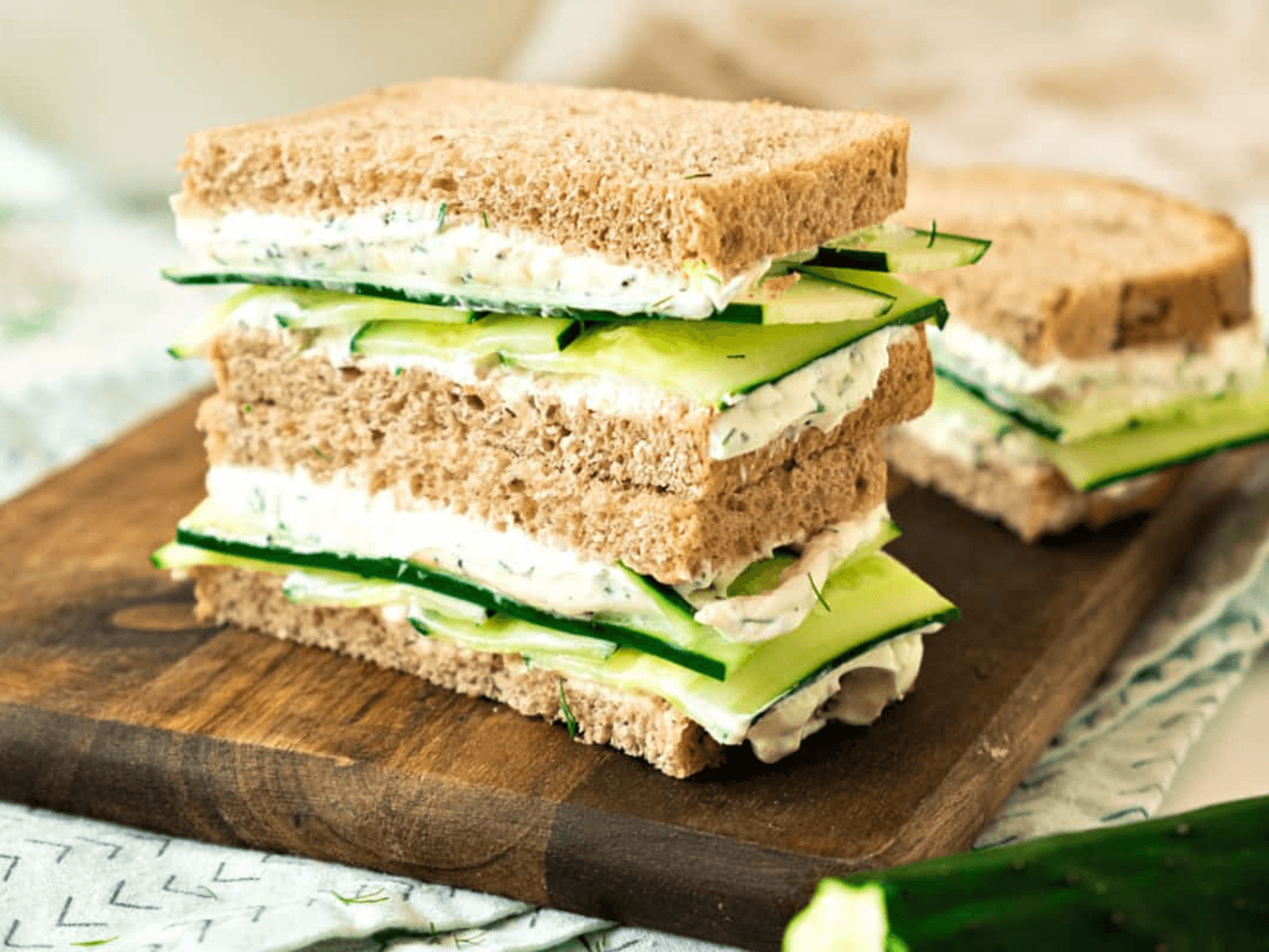 photo of two Classic Cucumber Dill Sandwiches on a wooden cutting board
