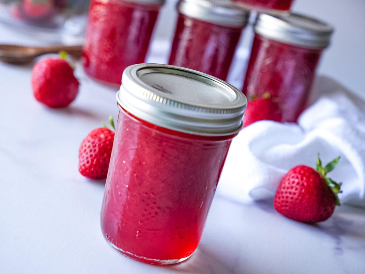 side view photo of strawberry jam in the foreground with more blurred in the background
