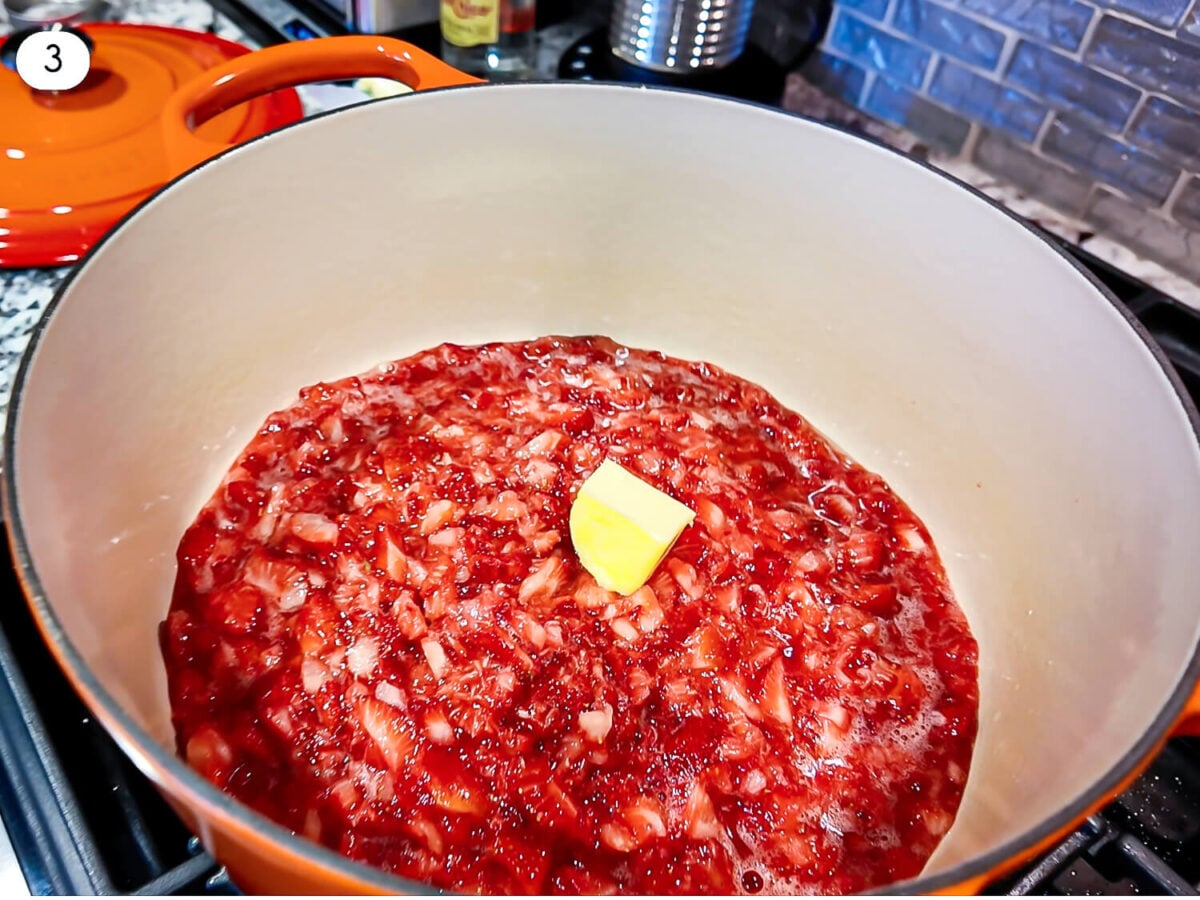 step 3 photo of mashed up strawberries in a dutch oven with a cube of butter