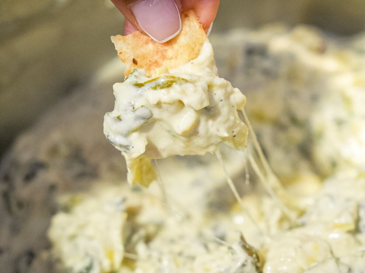close up photo of Crockpot Spinach and Artichoke Dip being scooped out of a crockpot