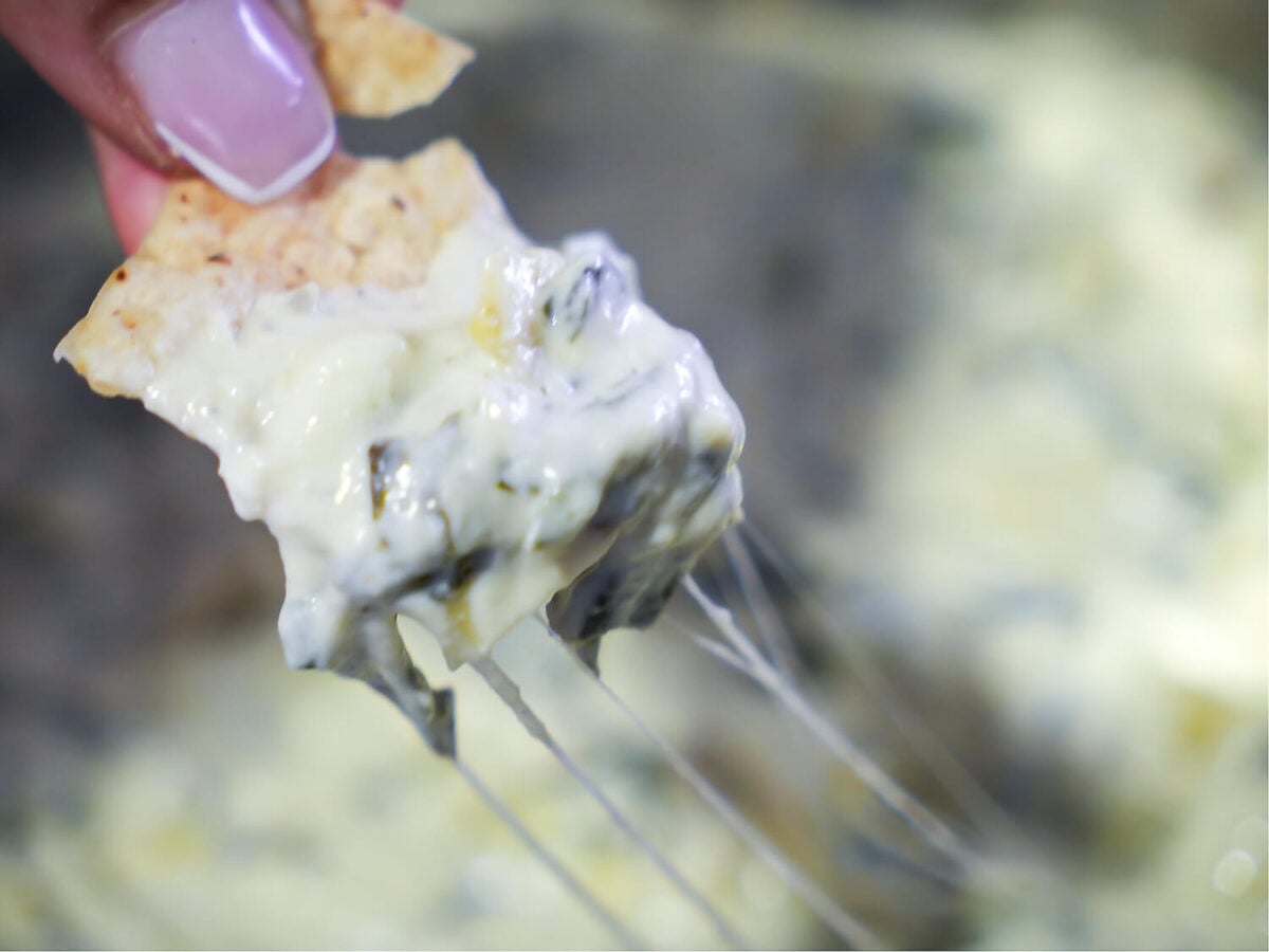 close up photo showing a cheese pull of the Crockpot Spinach and Artichoke Dip