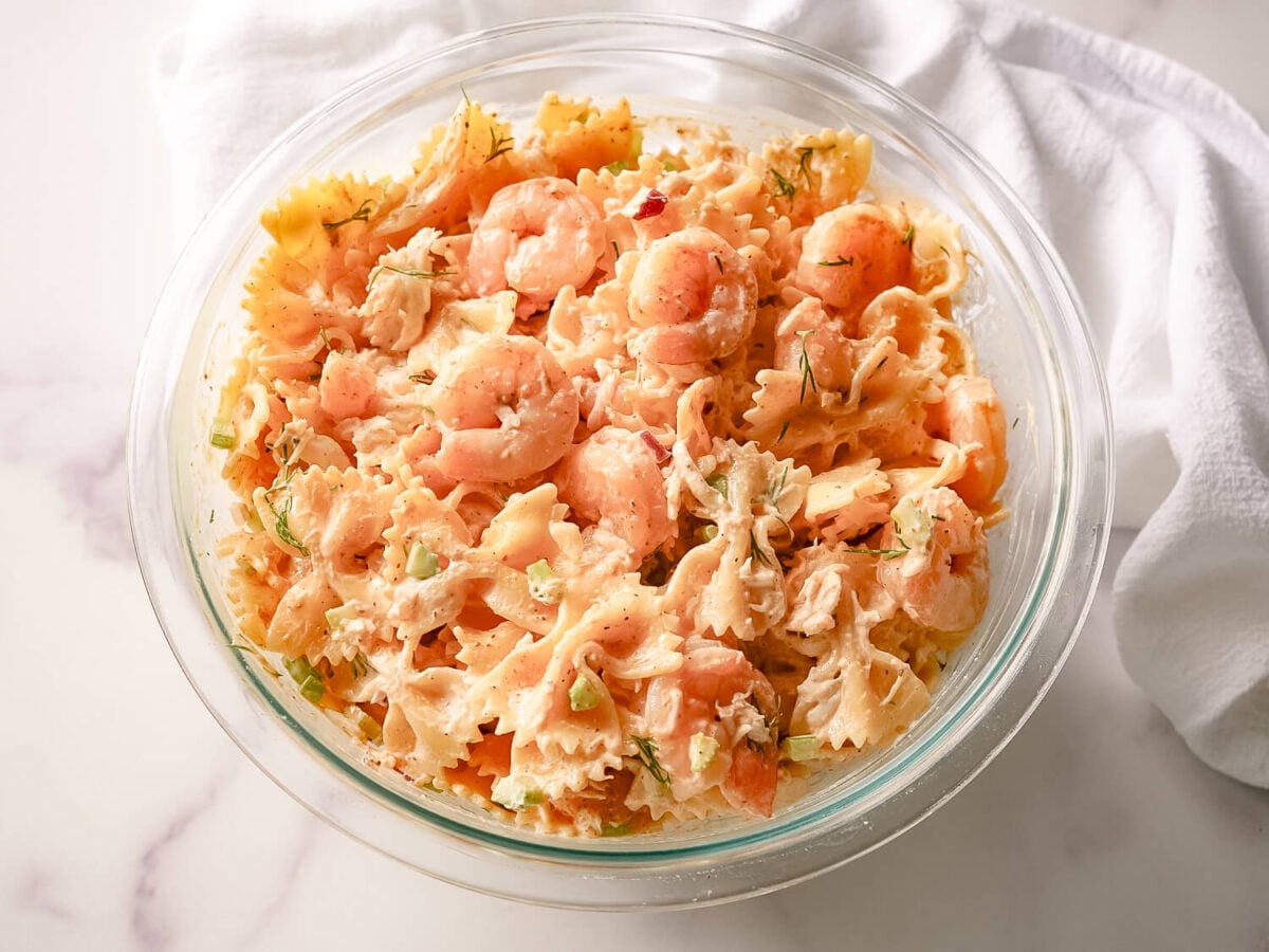 overhead photo of Seafood Pasta Salad in a glass bowl next to a white linen napkin