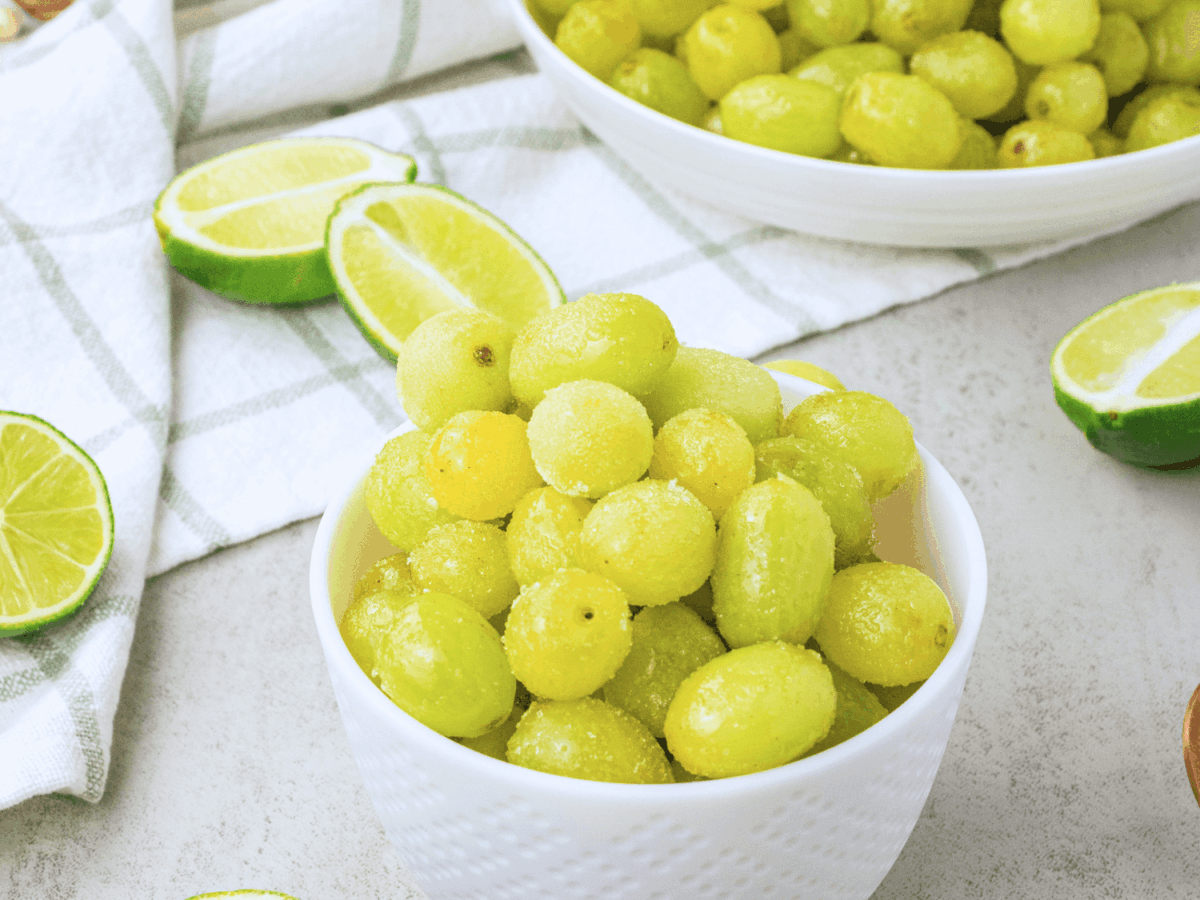overhead photo of Sour Patch Grapes in a small bowl surrounded by limes