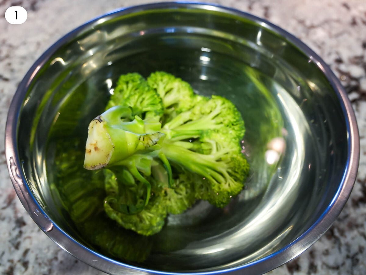 step 1 photo of a broccoli head being cleaned in salt water
