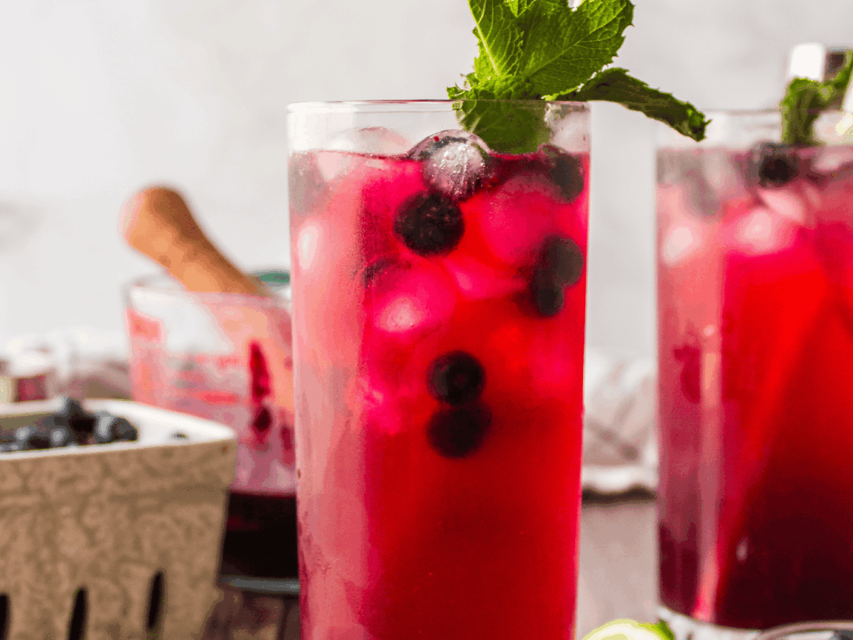 close up photo of a blueberry mojito with one in the background