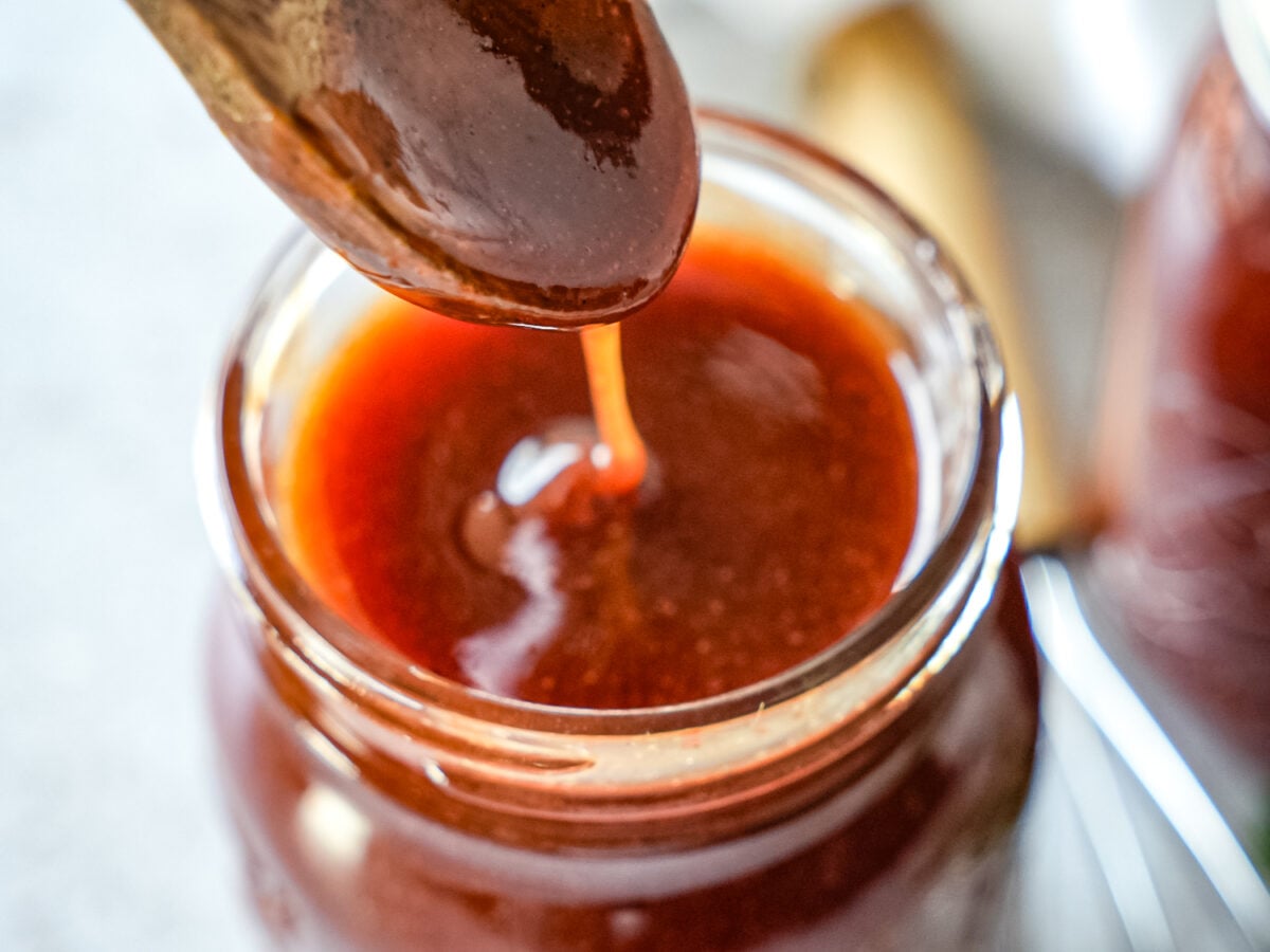 close up photo of honey bbq sauce dripping off a spoon into a jar