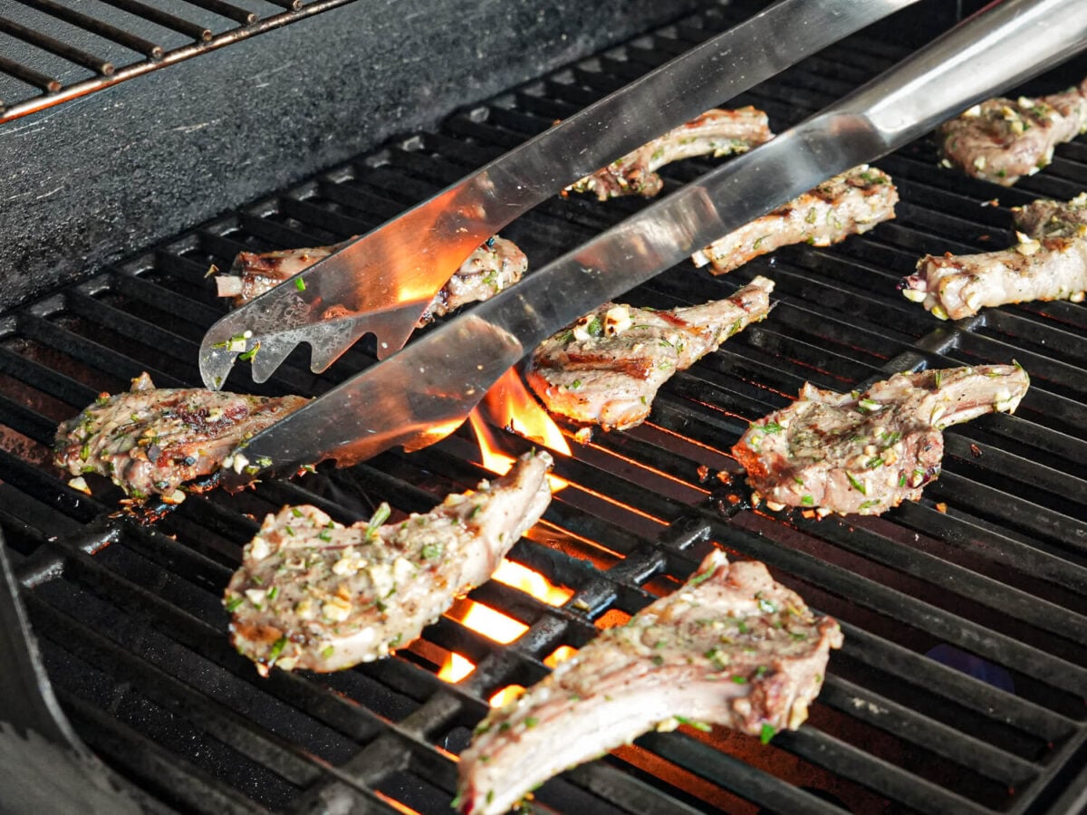 photo of lamb chops being flipped with metal tongs on the grill