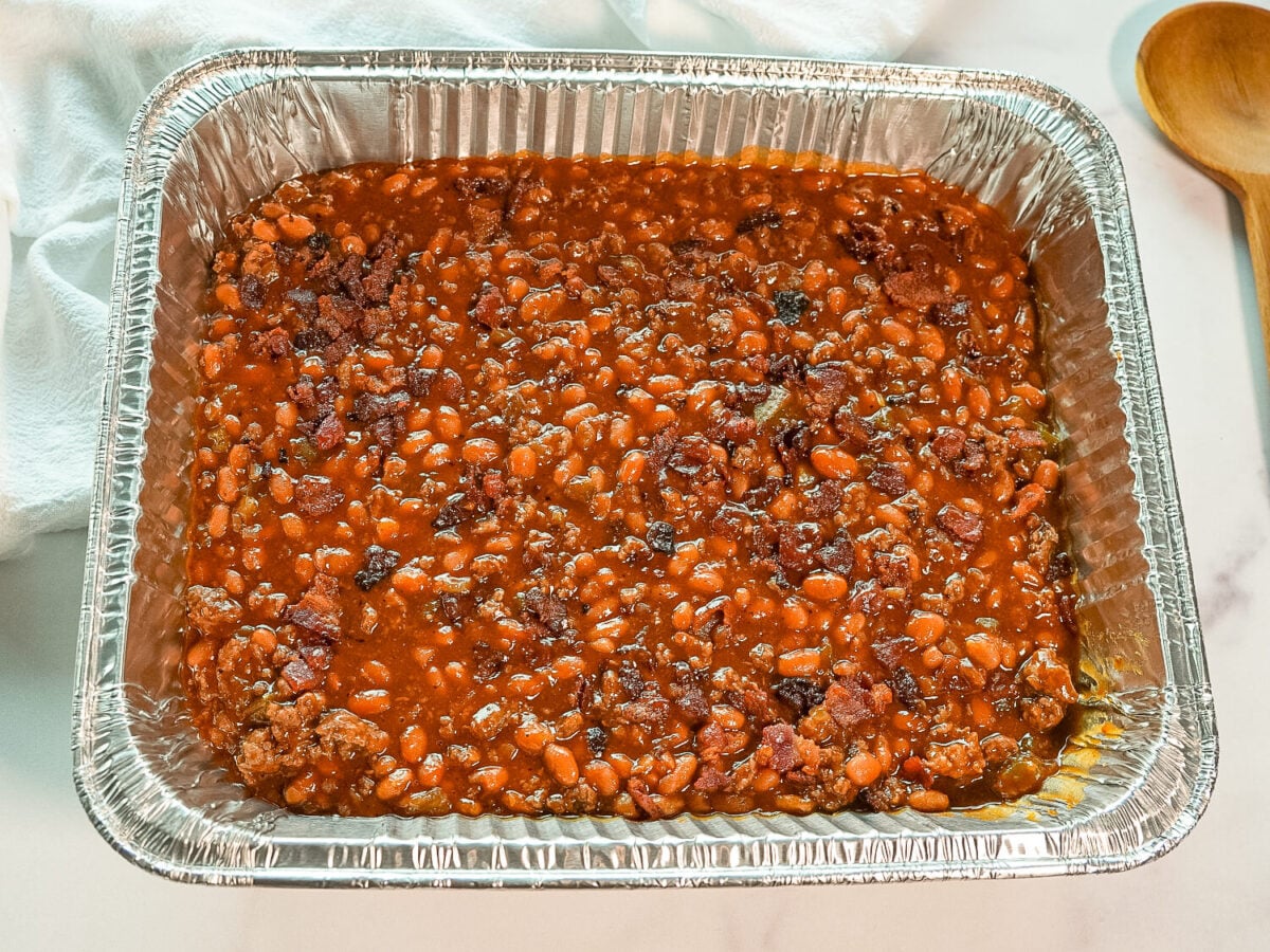 photo so baked beans in a metal pan next to a wooden spoon