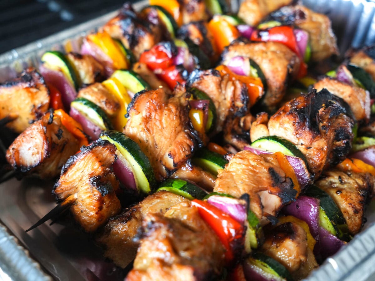 overhead photo showing cooked grilled chicken kabobs resting in a metal pan