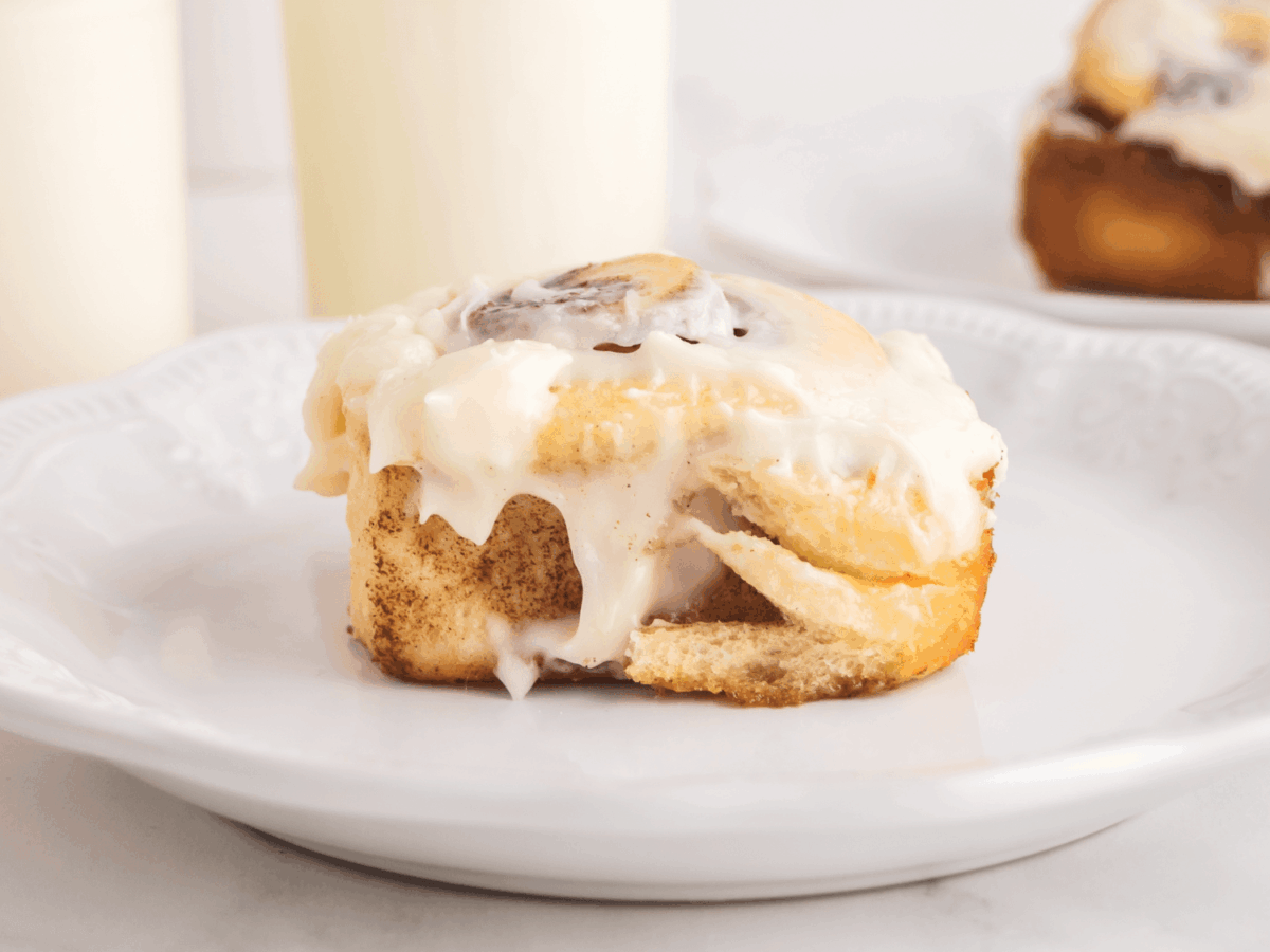 photo of a single cinnamon roll on a white plate with a cup of milk in the background