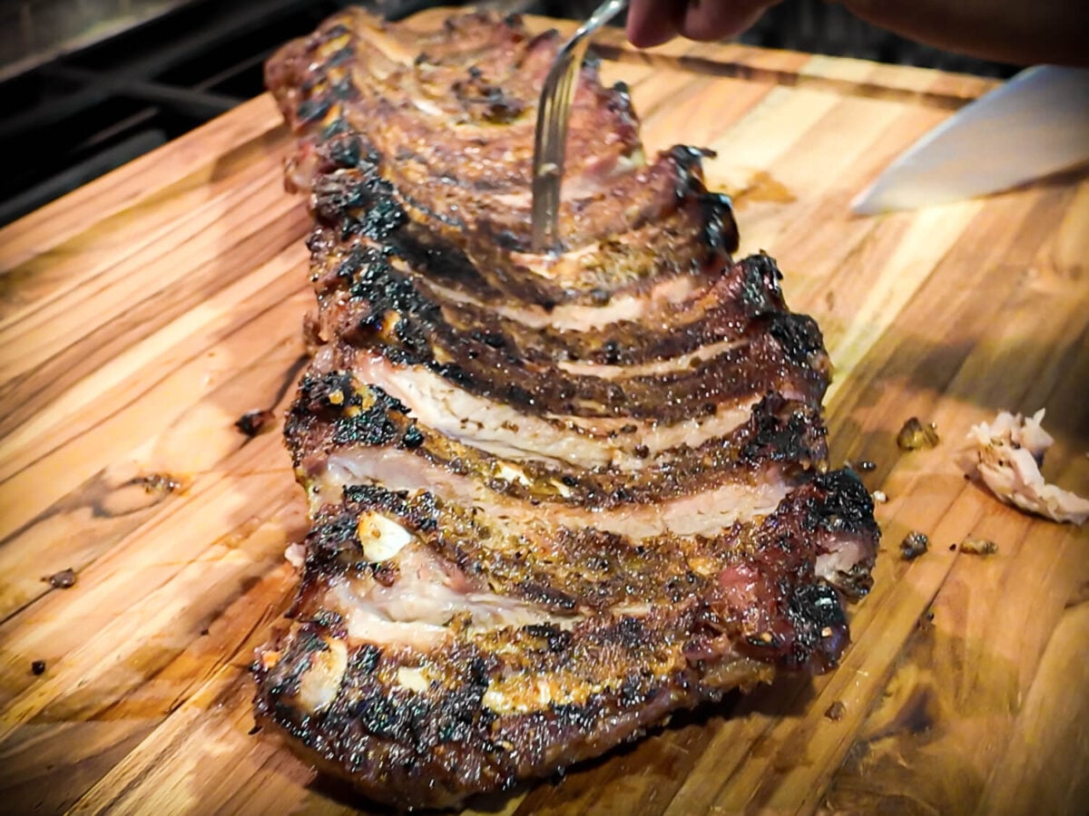 photo showing BBQ Baby Back Ribs being cut on a wooden cutting board