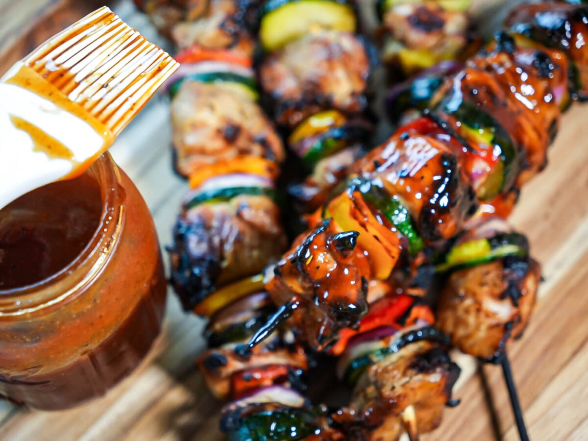 photo showing a cooked grilled chicken kabob next to a mason jar and brush of honey bbq sauce