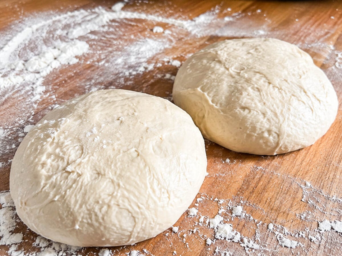 photo showing two easy pizza dough balls on a wooden surface