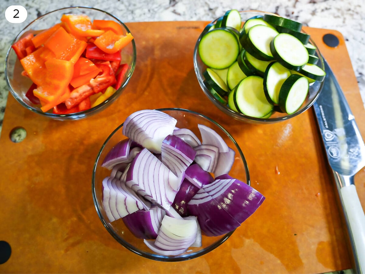 step 2 photo showing chopped peppers, zucchini, and red onions in glass bowls