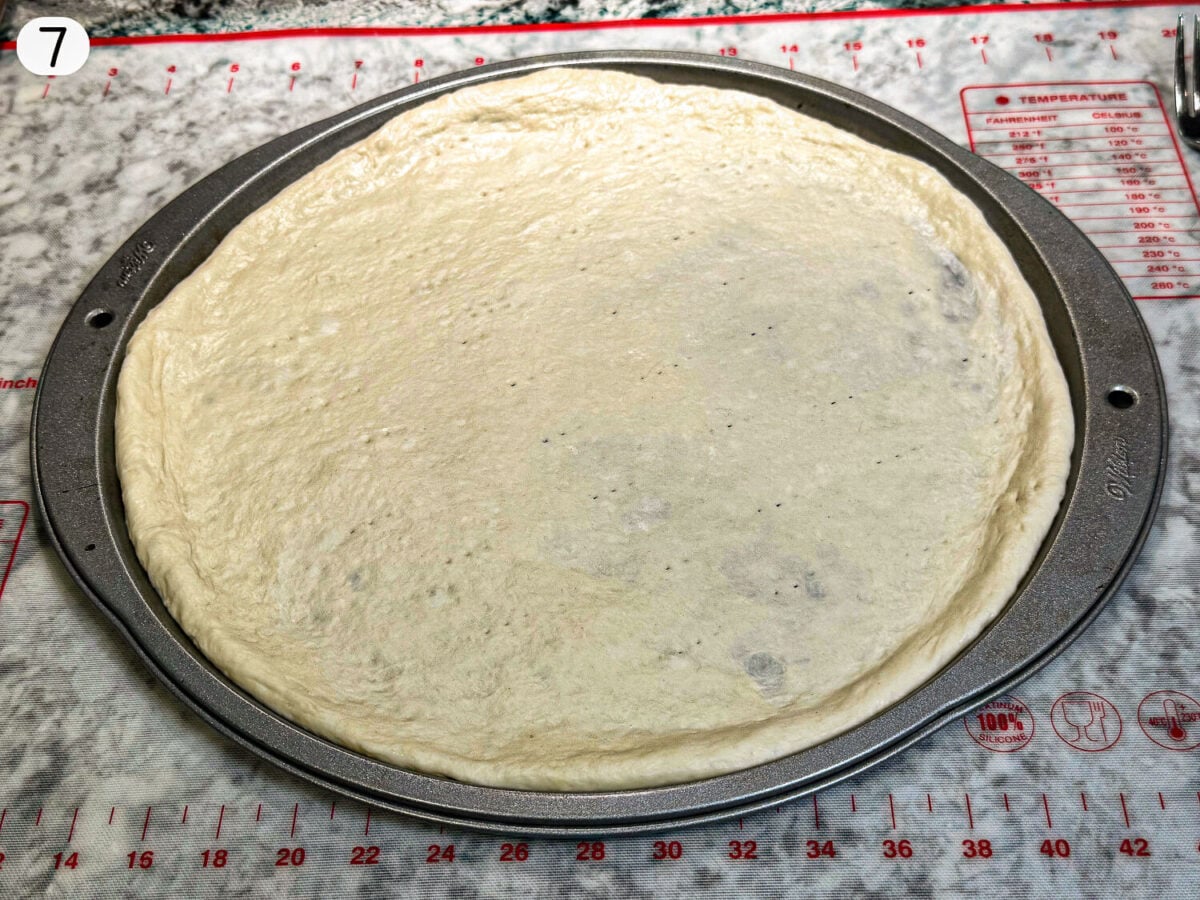 step 7 photo showing pizza dough in a pan before its baked