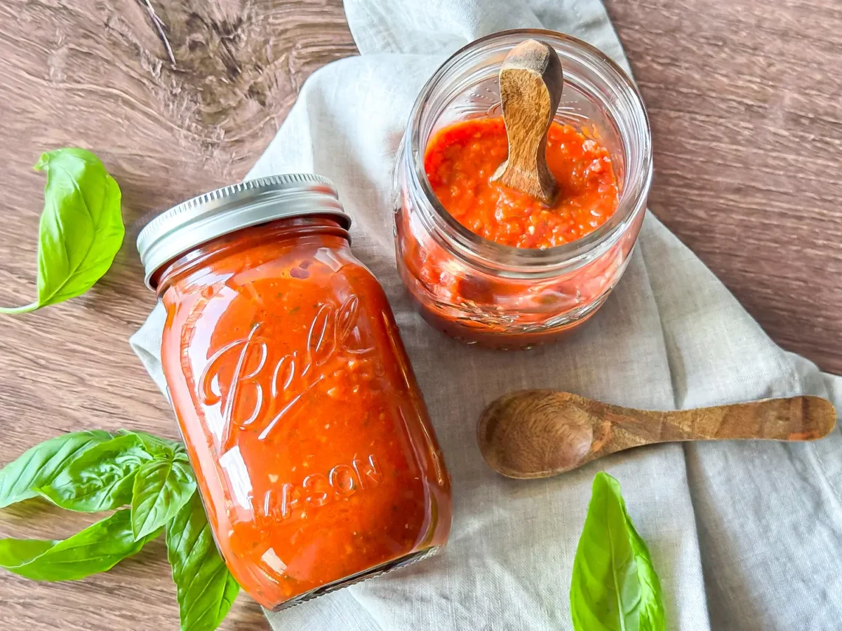 HERO Two glass mason jars filled with homemade marinara sauce are arranged on a light cloth with fresh basil leaves and wooden spoons v2