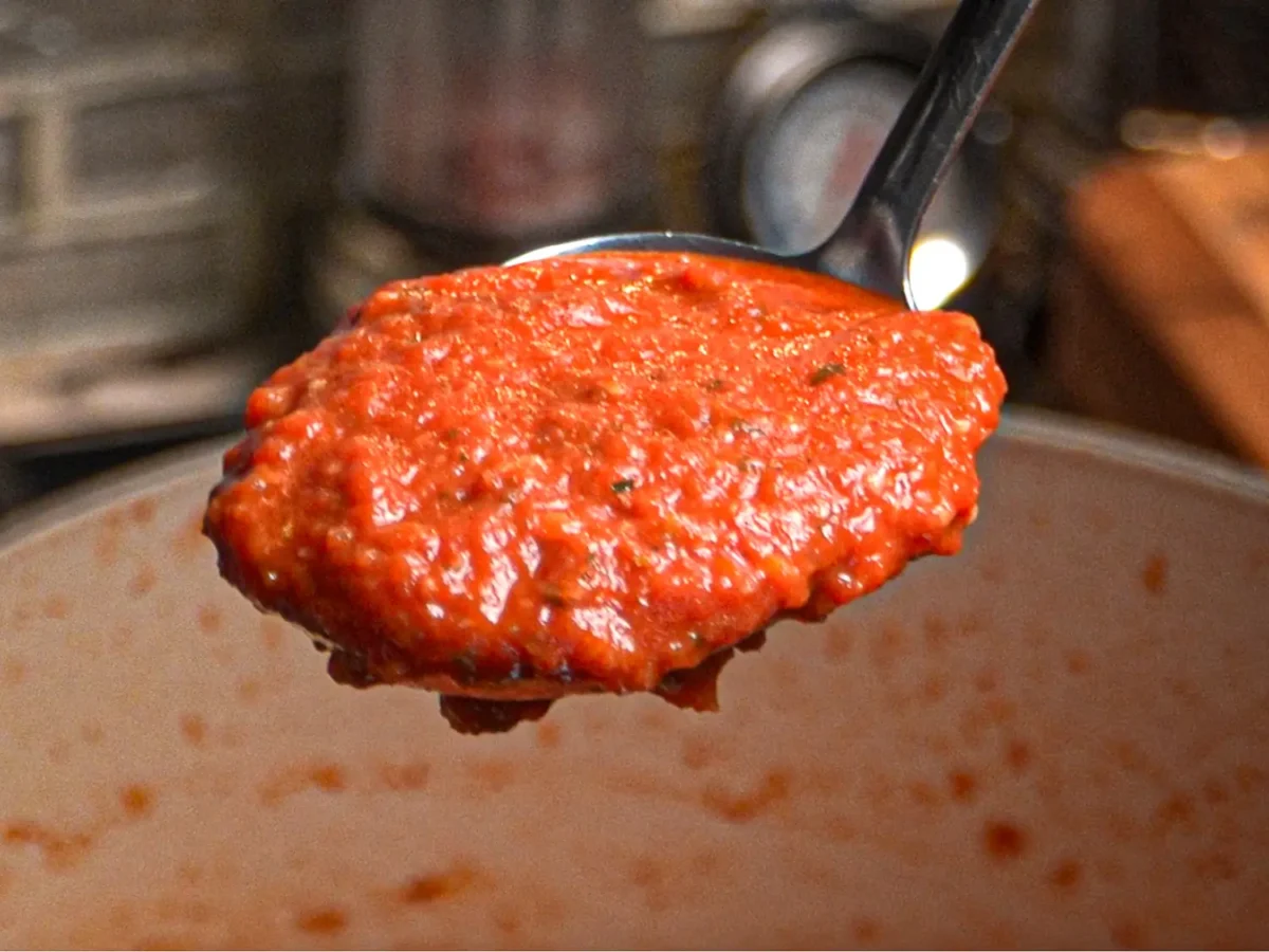 A close-up of a ladle filled with thick homemade marinara sauce, showing its rich tomato color and slightly chunky texture