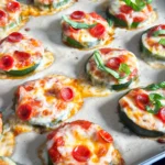 Baked zucchini pizza bites topped with marinara sauce, melted mozzarella cheese, mini pepperoni, and fresh basil on a parchment-lined baking sheet