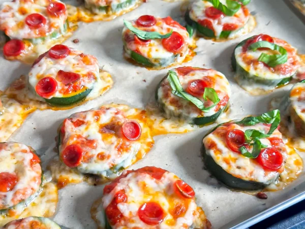 Baked zucchini pizza bites topped with marinara sauce, melted mozzarella cheese, mini pepperoni, and fresh basil on a parchment-lined baking sheet