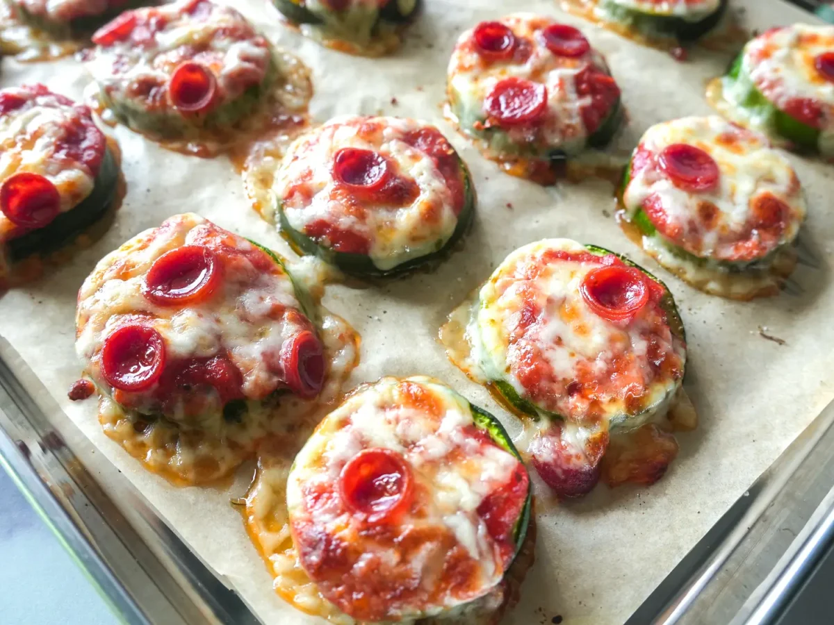 Close-up of baked zucchini pizza bites topped with marinara sauce, melted mozzarella cheese, and mini pepperoni, arranged on a parchment-lined baking sheet