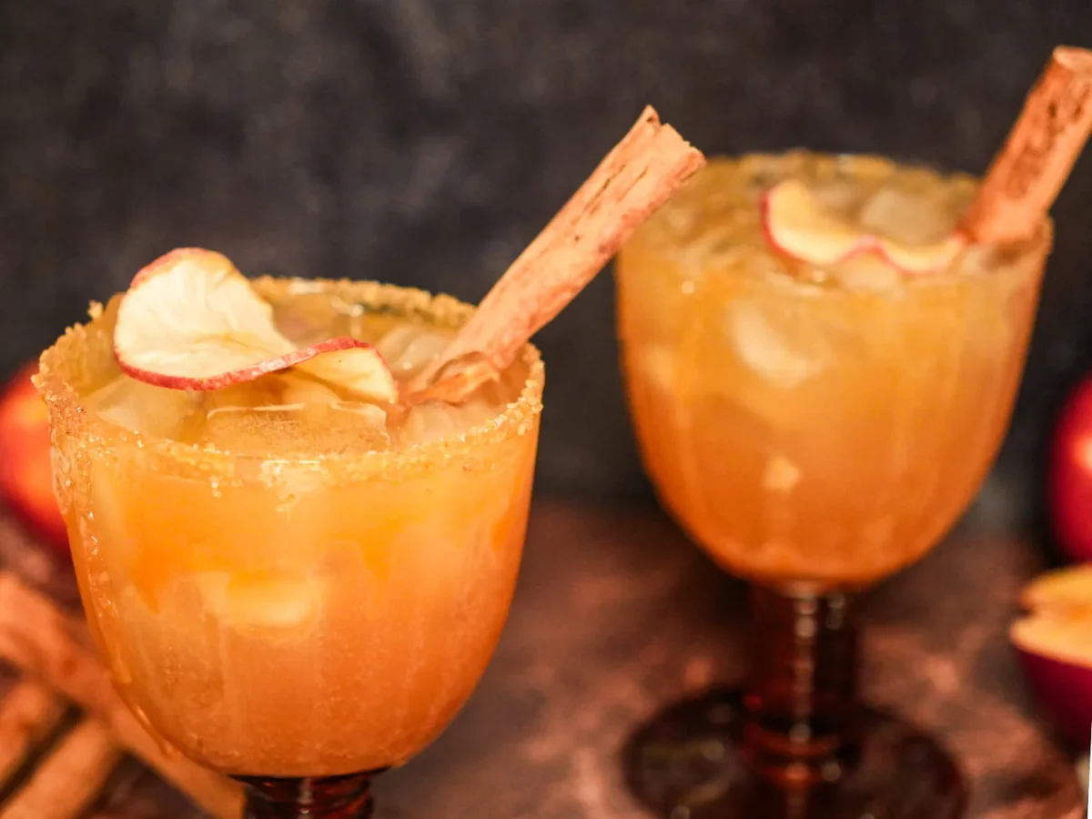 Close-up of two apple cider margaritas served over ice and garnished with dried apple slices and cinnamon sticks