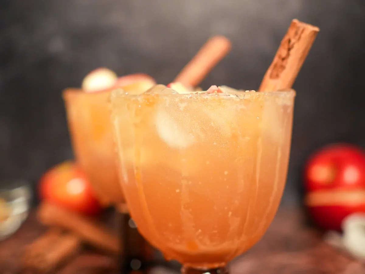 Finished apple cider margarita in an amber stemmed glass with a cinnamon-sugar rim, dried apple garnish, and cinnamon stick
