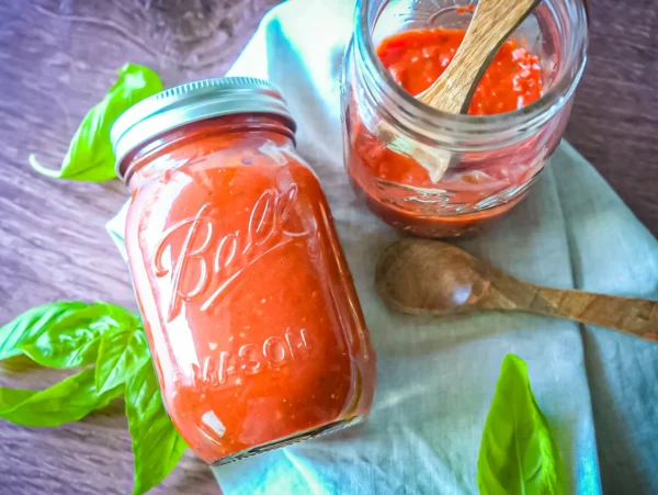 HERO Two glass mason jars filled with homemade marinara sauce are arranged on a light cloth with fresh basil leaves and wooden spoons