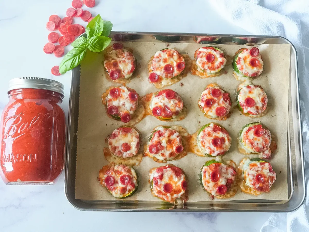 Overhead view of baked zucchini pizza bites topped with marinara sauce, melted mozzarella cheese, and mini pepperoni on a parchment-lined baking sheet