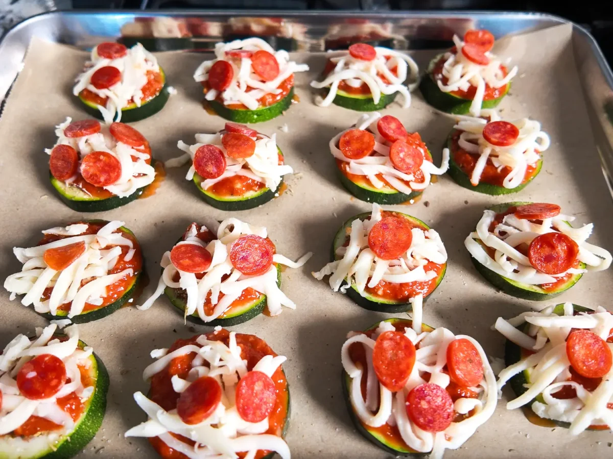 Unbaked zucchini pizza bites topped with marinara sauce, shredded mozzarella cheese, and mini pepperoni, arranged on a parchment-lined baking sheet and ready for the oven