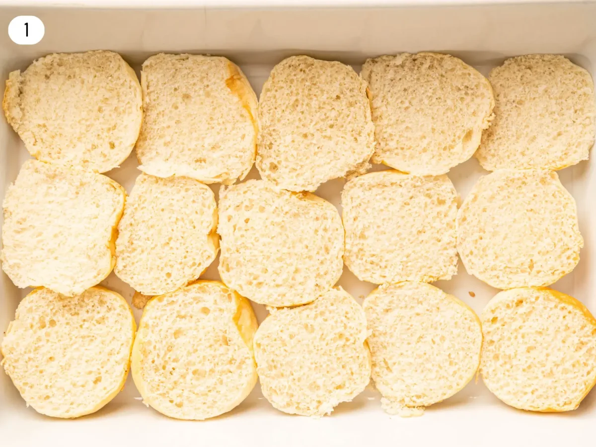 step 1 photo showing the hawaiian rolls cut in half before toppings are added in a white dish