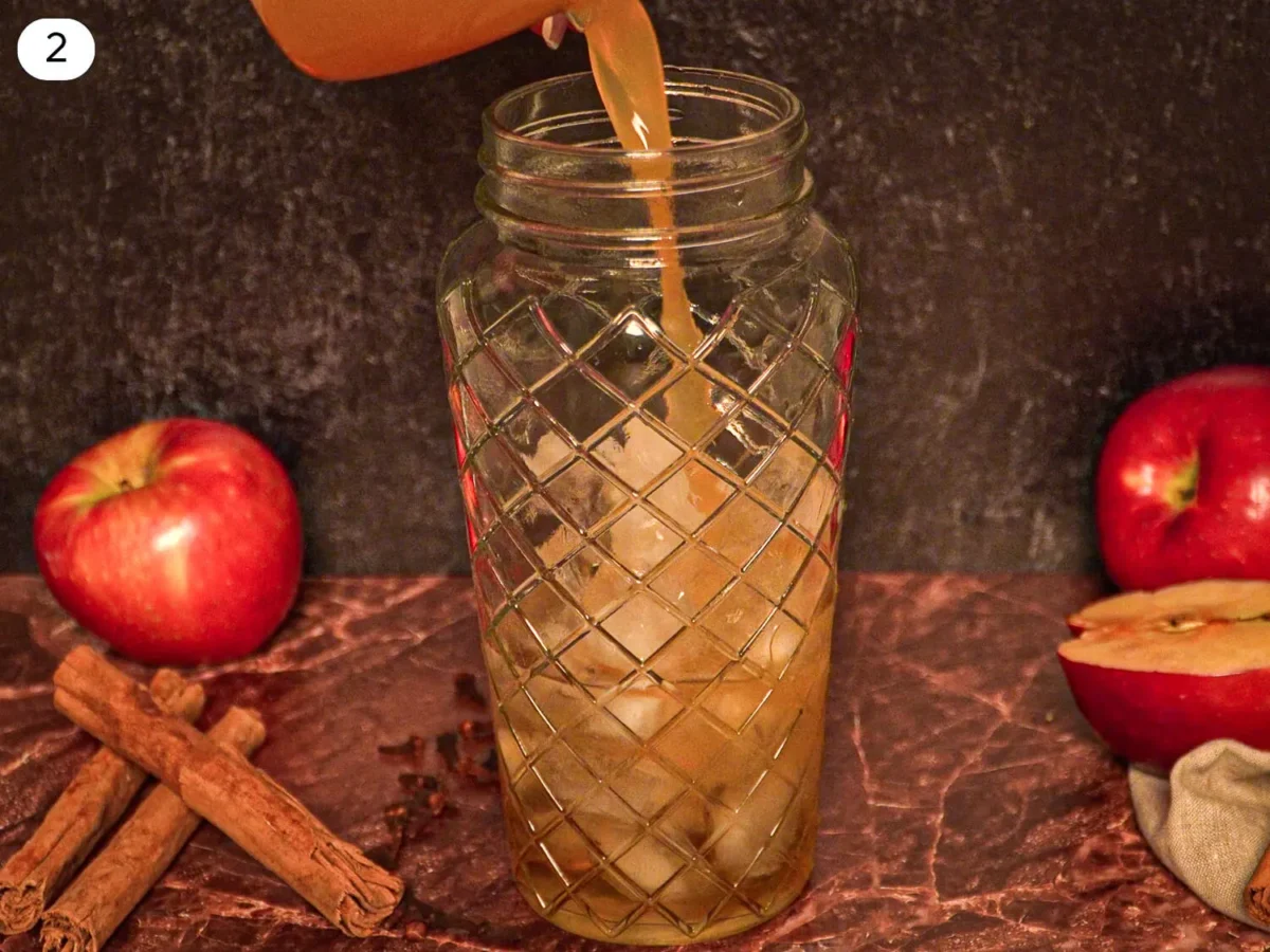 step 2 photo showing Fresh apple cider being poured into an ice-filled cocktail shaker while preparing an apple cider margarita