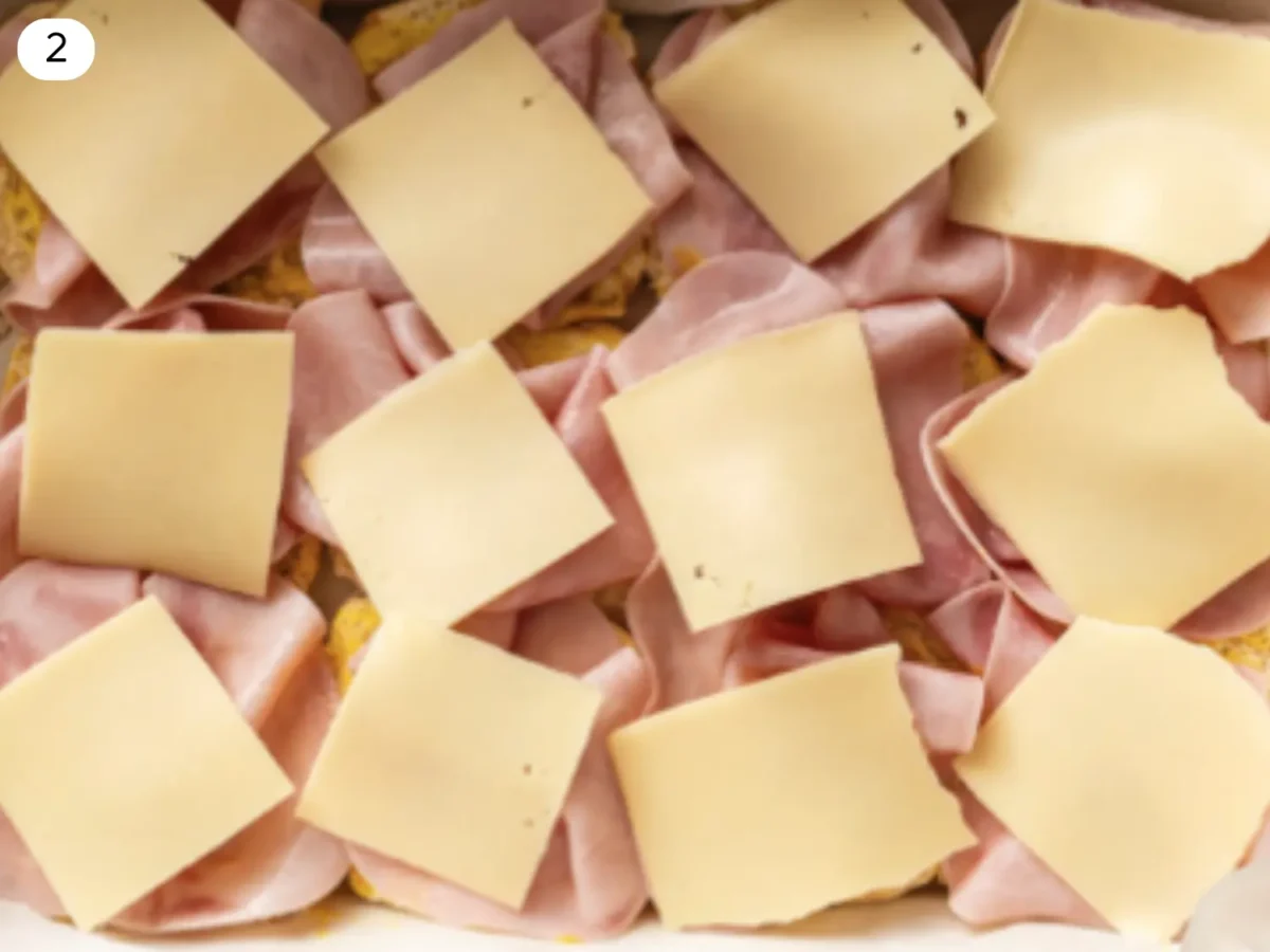 step 2 photo showing bottom part of rolls with honey mustard, ham and cheese on top before going in the oven