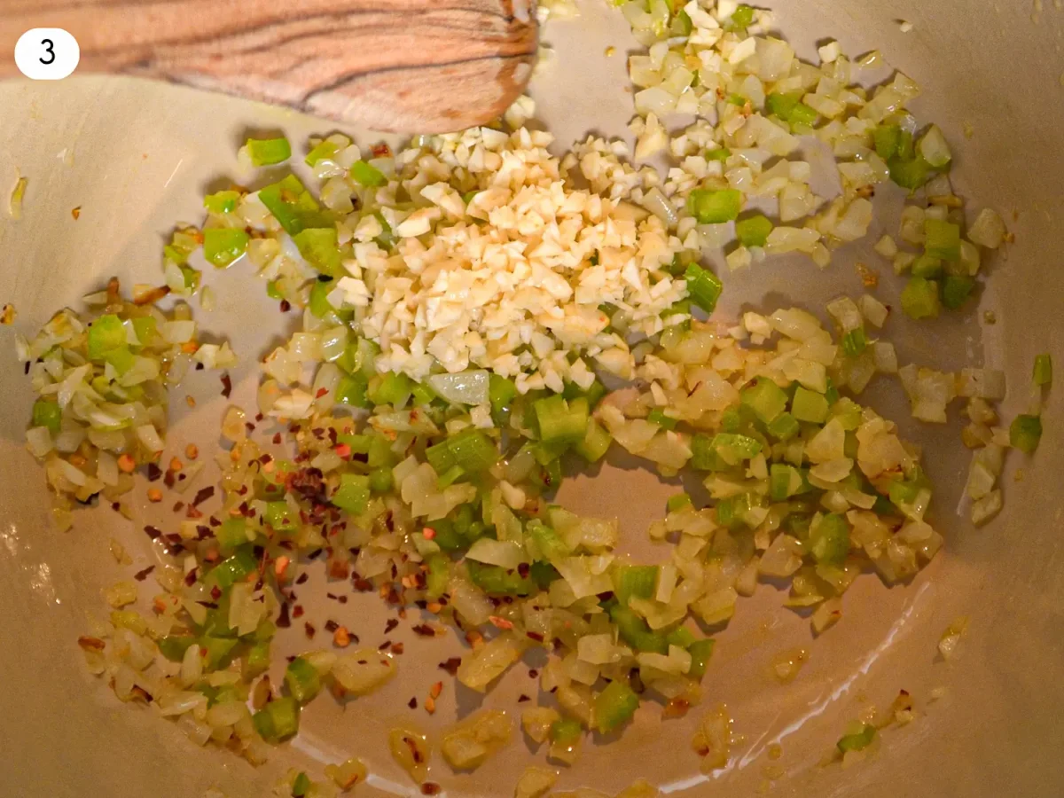 step 3 photo showing minced garlic and red pepper flakes blooming in the pot with celery and onions