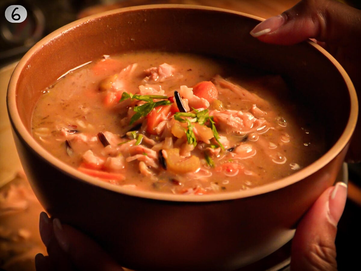step 6 photo showing the cooked chicken and wild rice soup in a brown bowl garnished with parsley