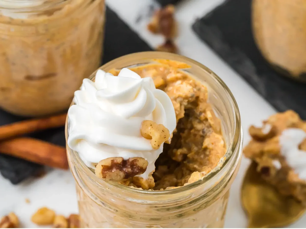 Close up photo of a pumpkin overnight oats with cream and nuts on top in a mason jar