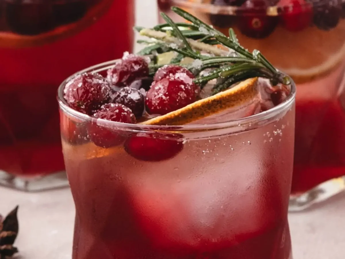 HERO Cranberry spritzer over ice, topped with sugared cranberries, a dried orange slice, and a sugared rosemary sprig