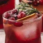 HERO Cranberry spritzer over ice, topped with sugared cranberries, a dried orange slice, and a sugared rosemary sprig