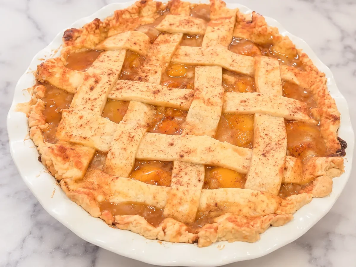 HERO homemade peach pie recipe in a white baking dish on a marble surface