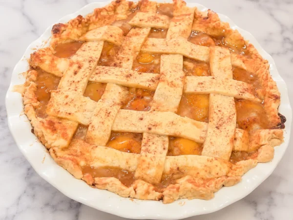 HERO homemade peach pie recipe in a white baking dish on a marble surface